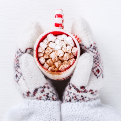 mittened hands holding mug of hot chocolate with marshmallows